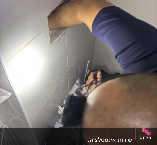 אדם עובד על צנרת בתוך קיר בחדר אמבטיה
